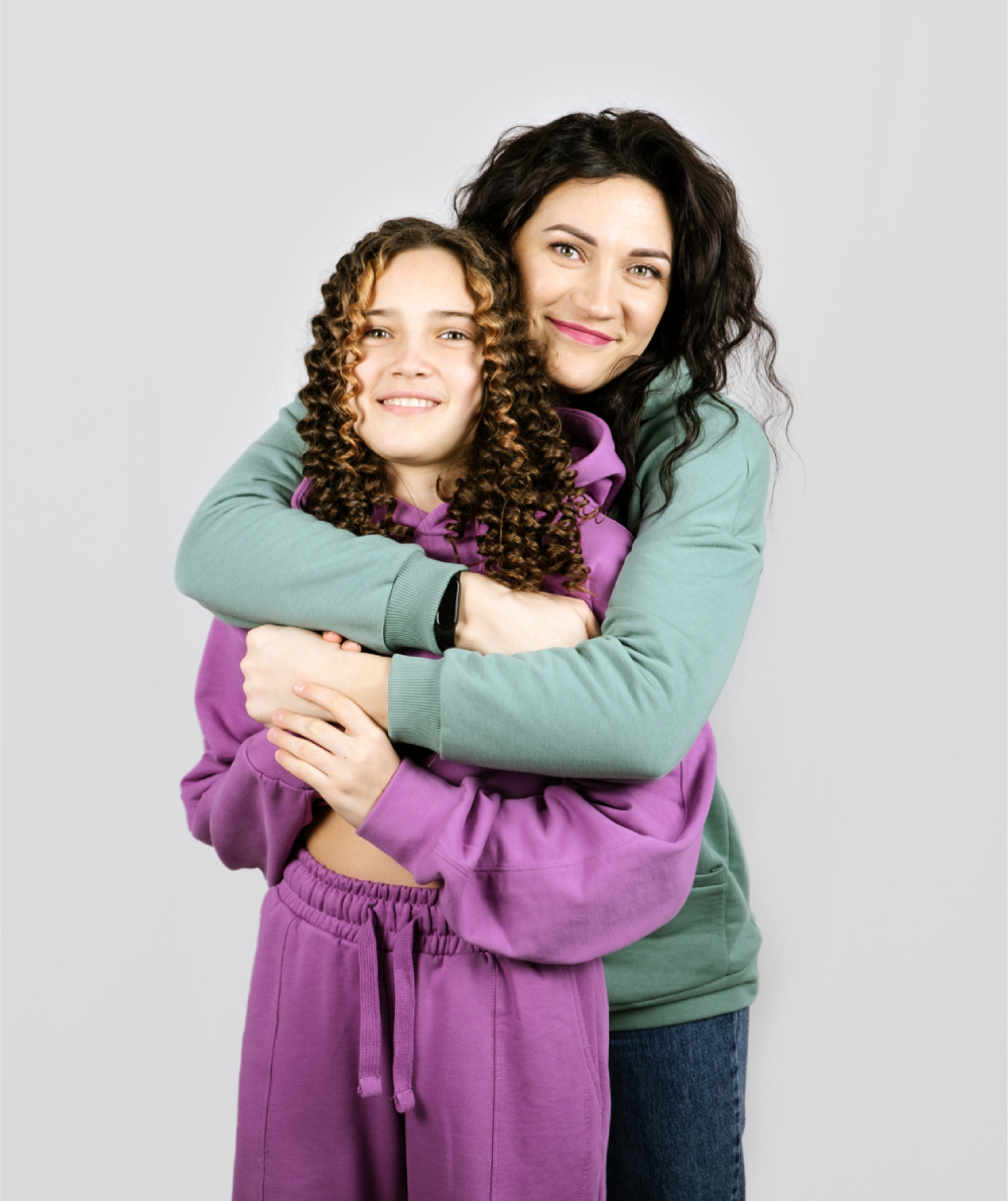 Smiling mother hugging teenage daughter from behind, both in casual clothing