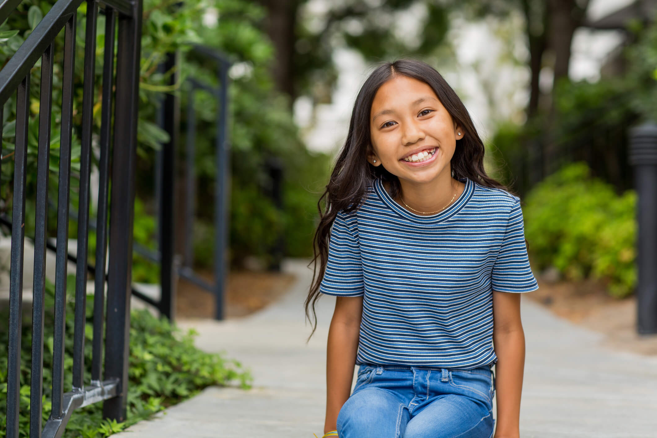 Smiling girl with braces in a striped shirt sitting outdoors on a sidewalk