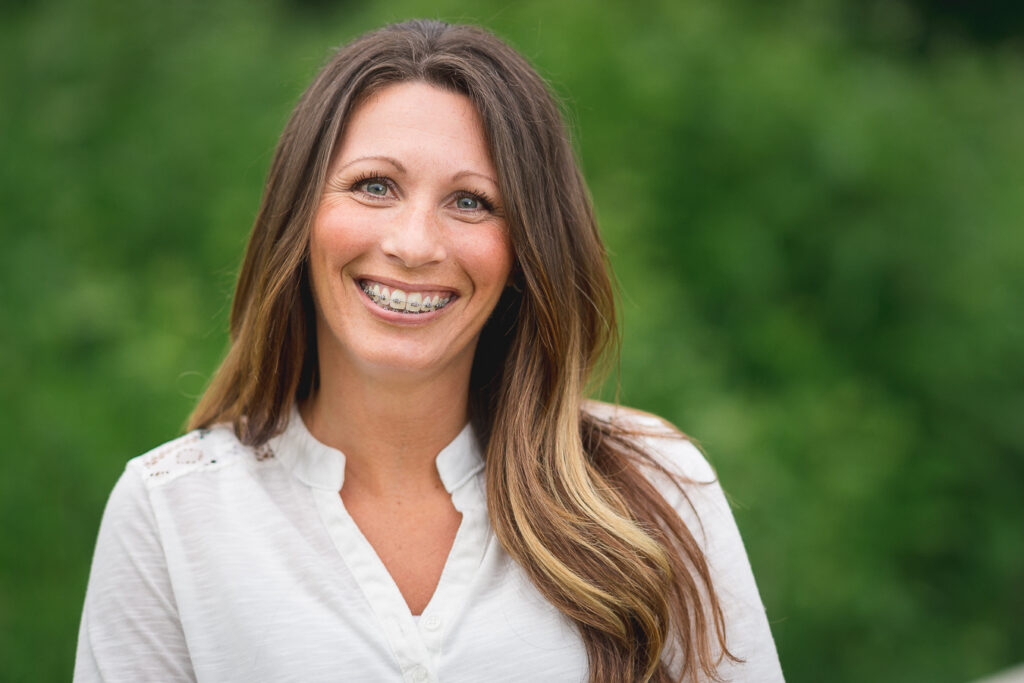 Smiling woman with long brown hair and braces, wearing a white blouse outdoors