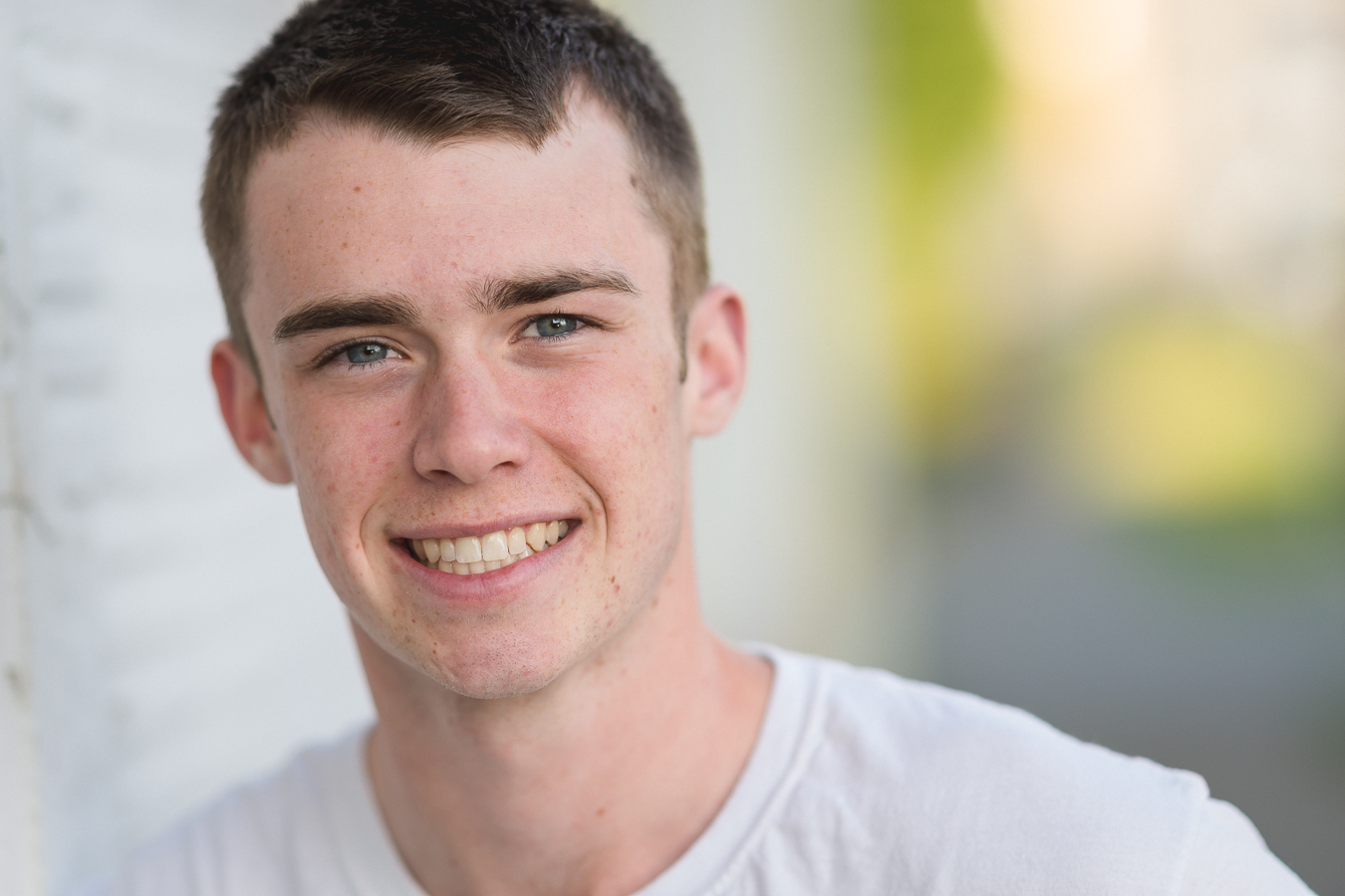 Smiling young man with short brown hair and white t-shirt showing straight teeth