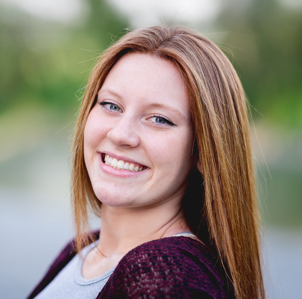 Smiling young woman with long auburn hair showing straight white teeth outdoors