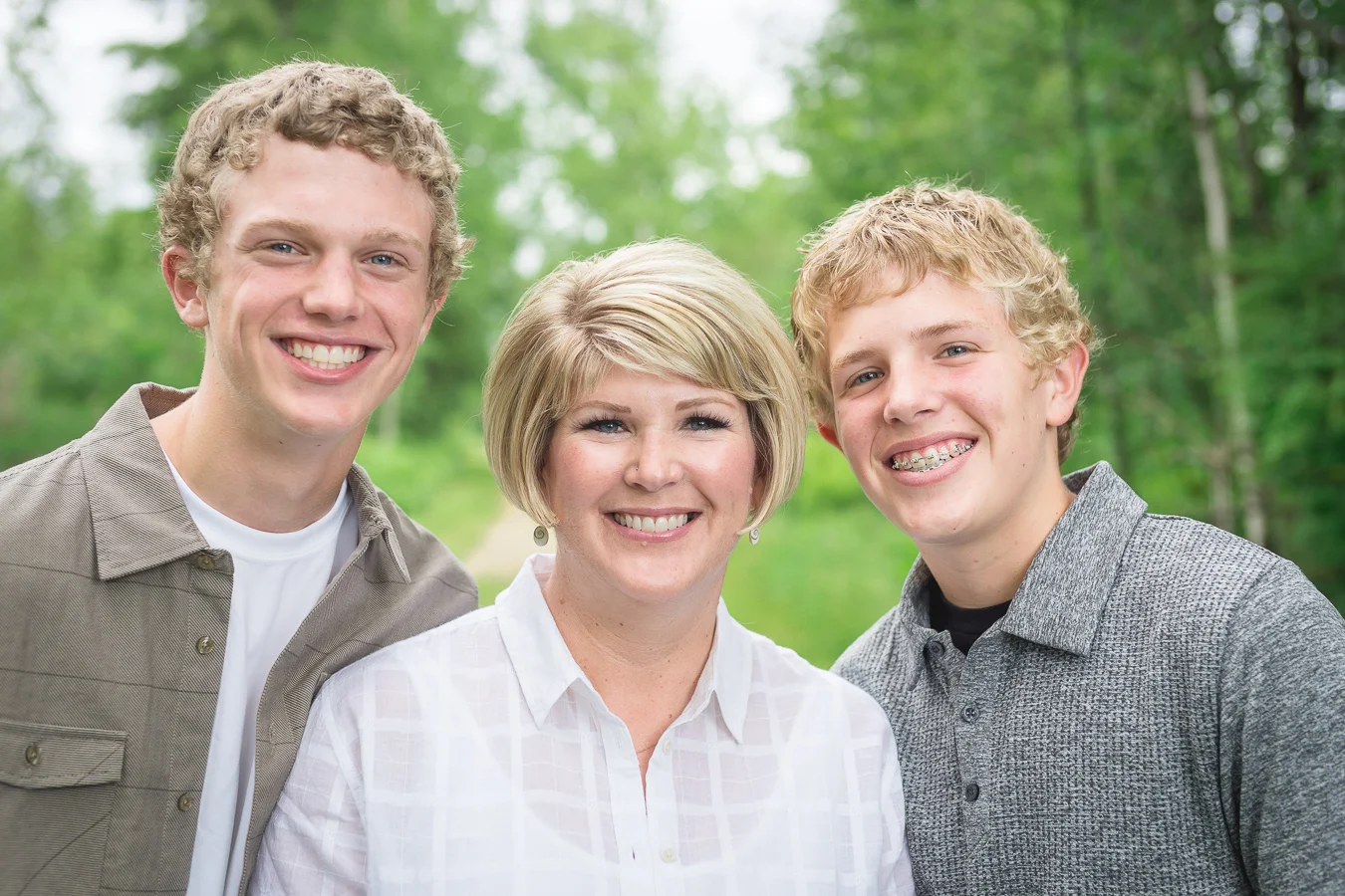 Smiling mother with two teenage sons posing outdoors among green trees