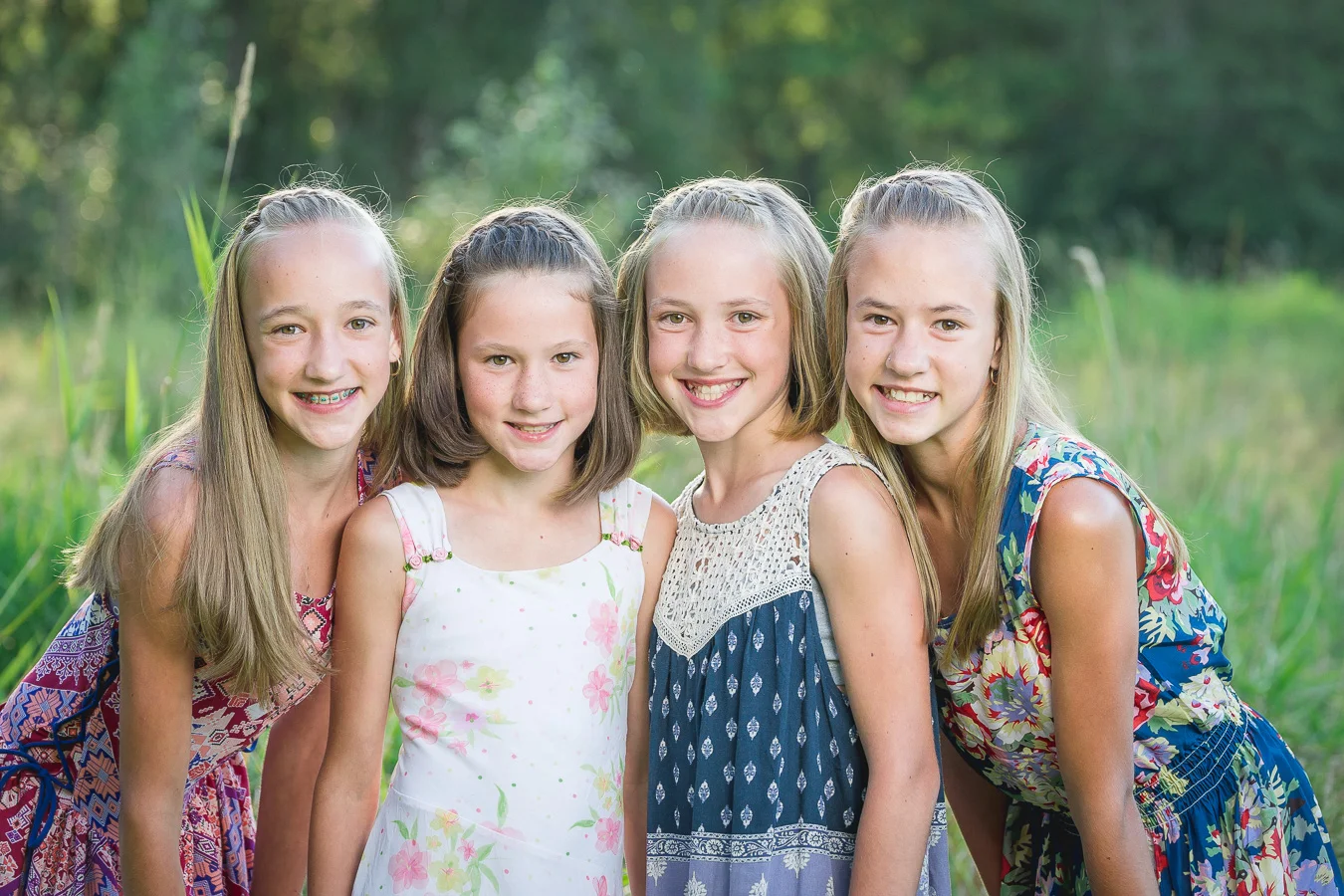 Four smiling young girls in summer dresses posing together outdoors