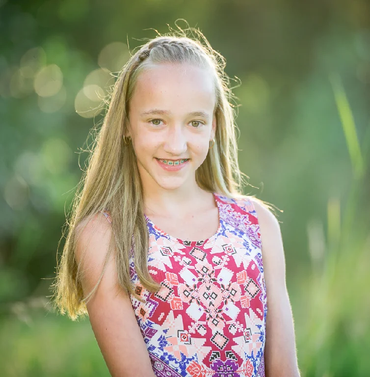 Smiling girl with long blonde hair and braces, wearing a patterned tank top outdoors