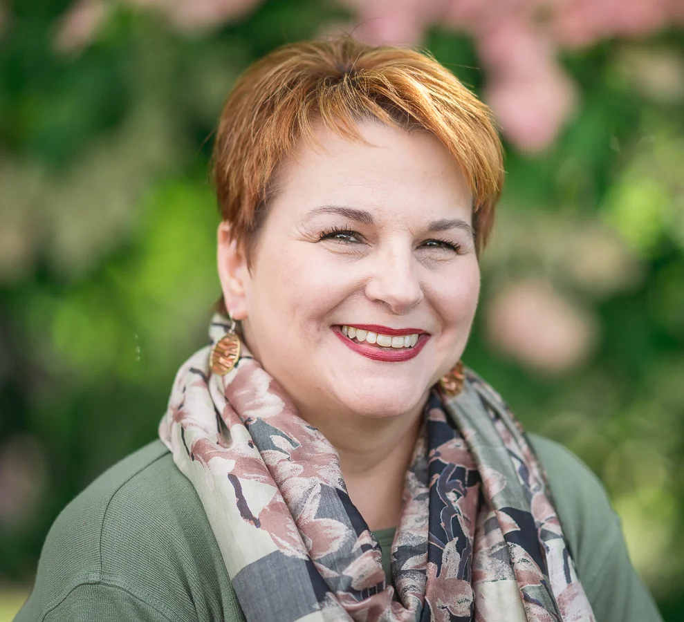 Smiling adult woman with short red hair, floral scarf, showing straight white teeth outdoors