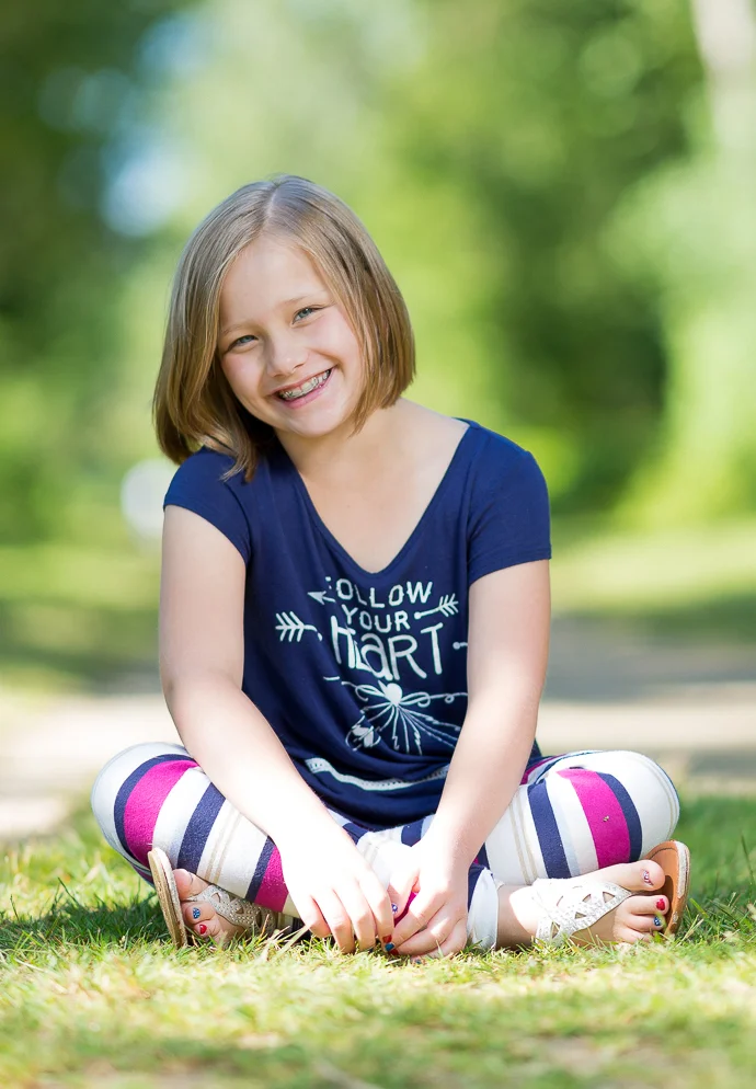 Smiling girl with braces sitting cross-legged on grass in a sunny park