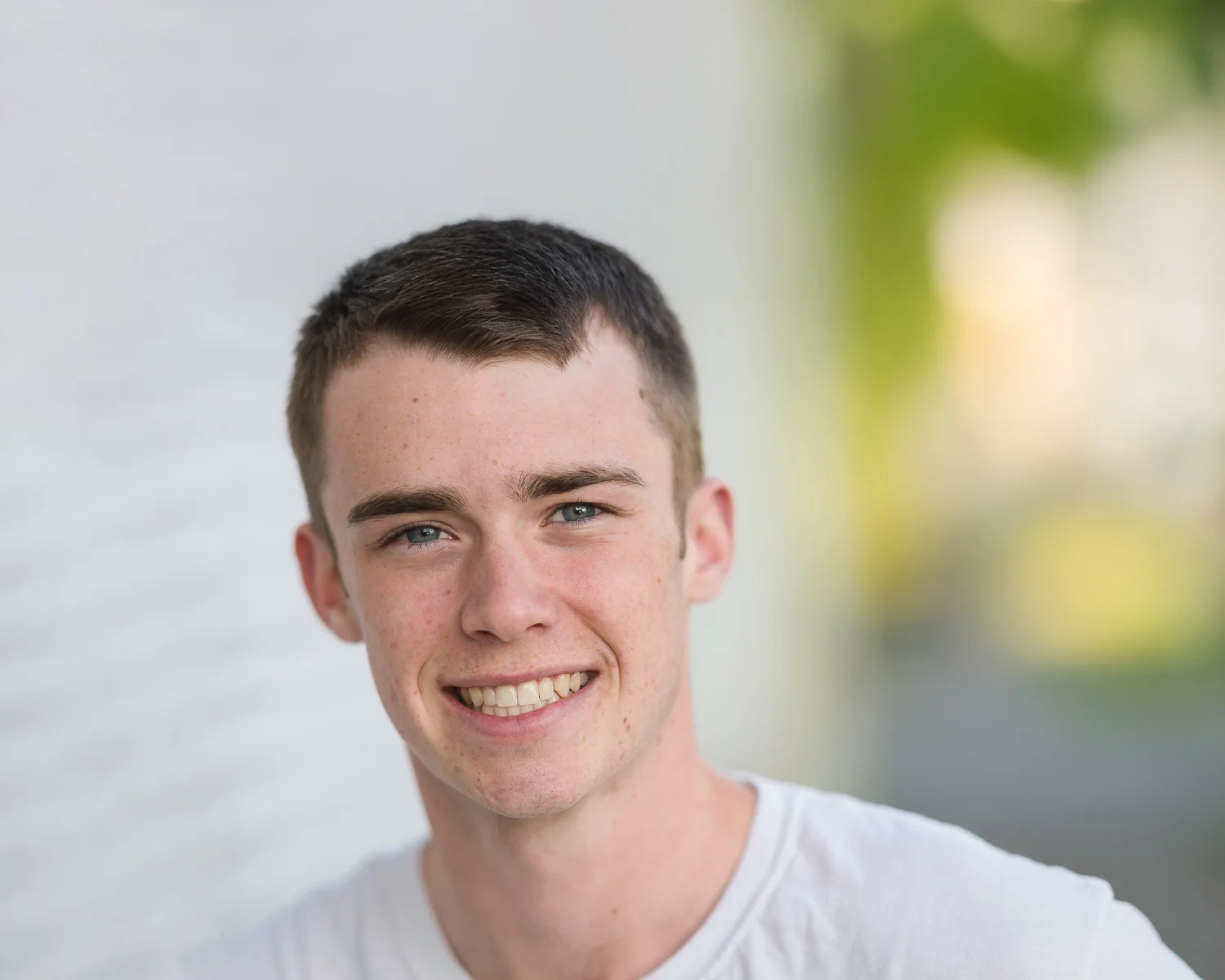 Smiling young man with short brown hair and straight teeth in a white t-shirt